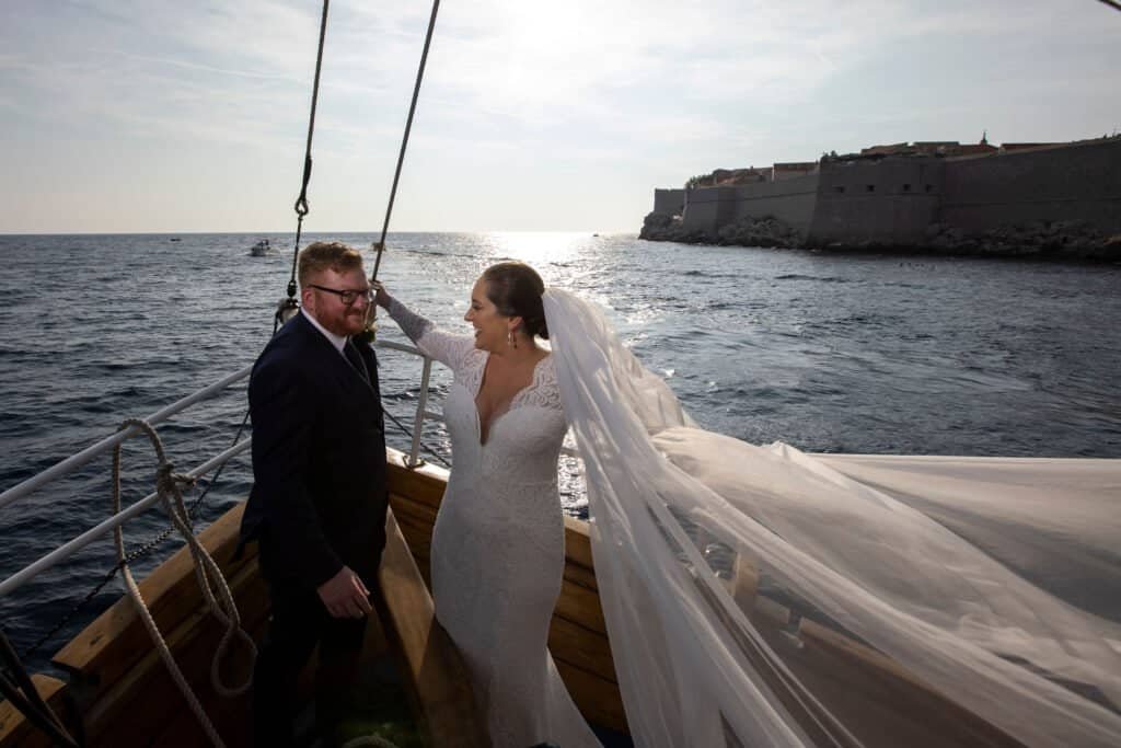 Joe and Lex in wedding suit and dress on a boat with the veil blowing in the wind